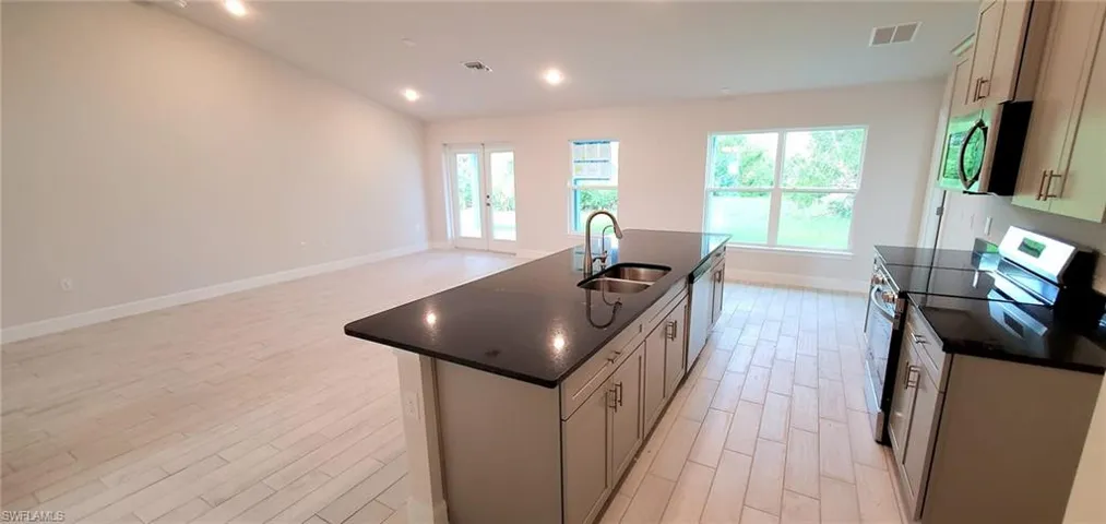 Kitchen featuring a center island with sink, dark stone counters, stainless steel appliances, light hardwood / wood-style floors, and sink