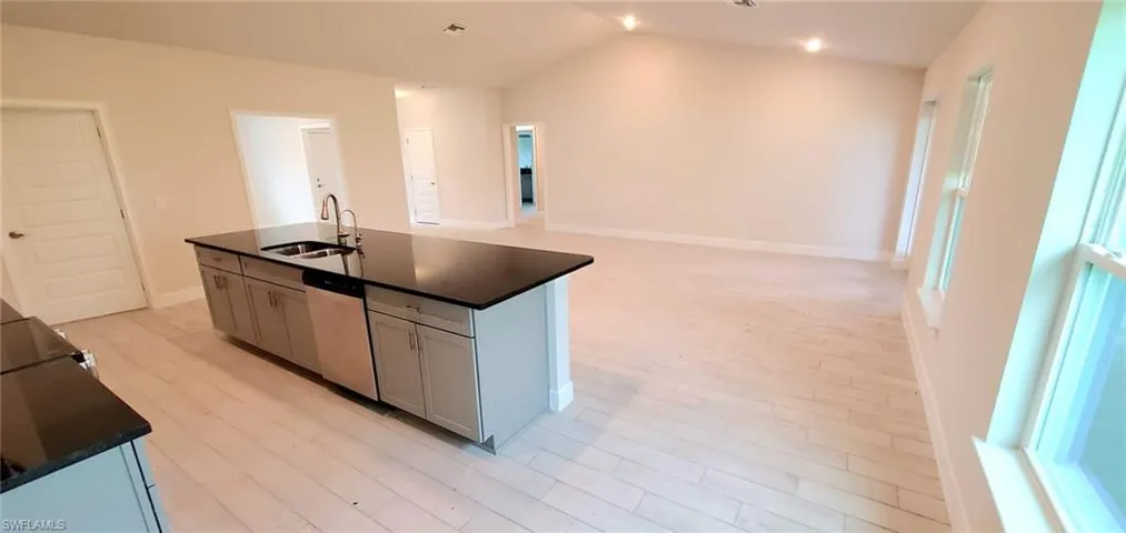 Kitchen featuring lofted ceiling, light hardwood / wood-style flooring, a kitchen island with sink, stainless steel dishwasher, and sink