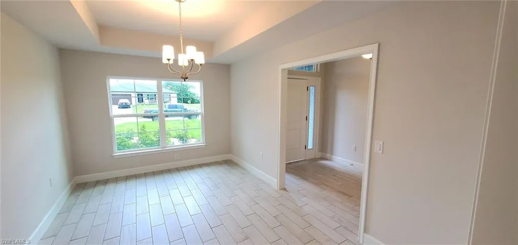 Spare room with an inviting chandelier, a raised ceiling, and light hardwood / wood-style floors