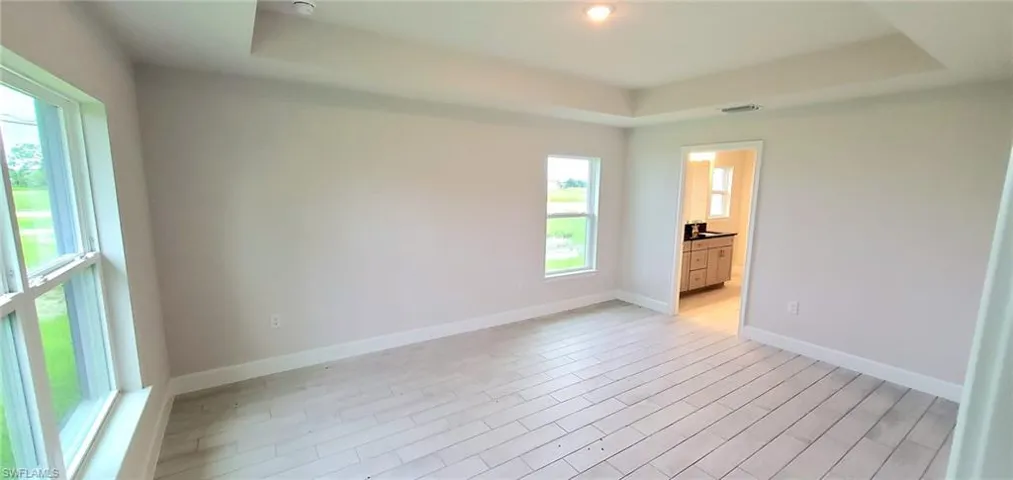 Unfurnished bedroom with light hardwood / wood-style floors, ensuite bath, and a tray ceiling