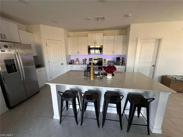Kitchen featuring stainless steel appliances, white cabinets, light stone countertops, and a kitchen bar