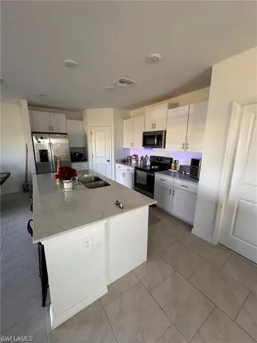 Kitchen featuring stainless steel appliances, an island with sink, light stone counters, light tile patterned floors, and white cabinetry