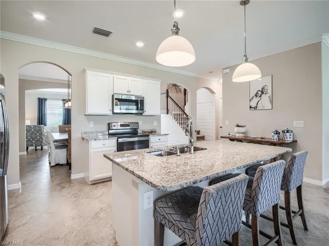 Kitchen featuring pendant lighting, sink, a kitchen bar, light stone countertops, and appliances with stainless steel finishes