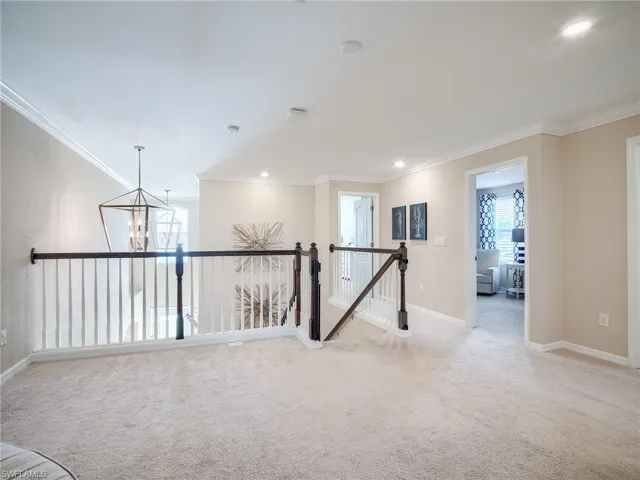 Carpeted spare room with an inviting chandelier, a healthy amount of sunlight, and ornamental molding
