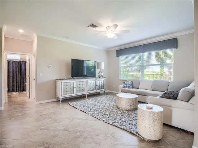 Living room featuring light tile patterned flooring, ceiling fan, and ornamental molding
