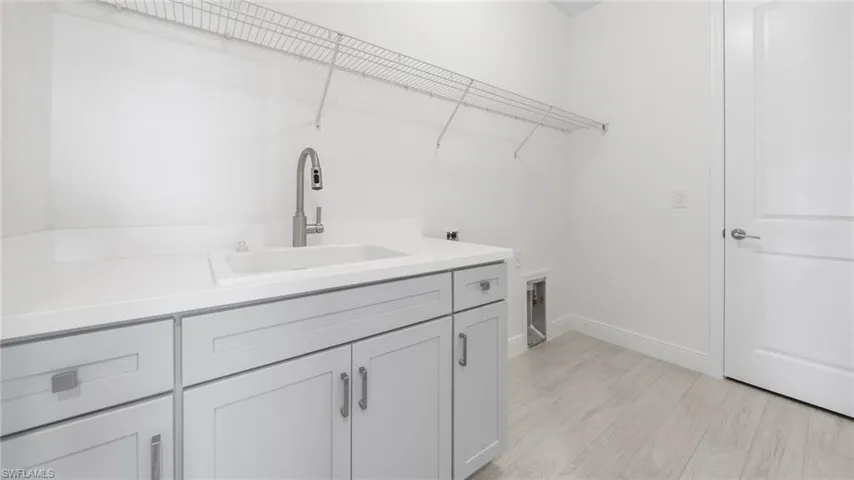 Laundry area featuring a utility sink with a modern faucet, white countertops, light gray cabinetry with brushed nickel hardware, and light wood-finish flooring
