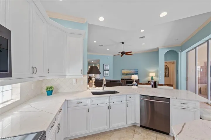Kitchen featuring ornamental molding, white cabinetry, light stone counters, stainless steel dishwasher, and a peninsula