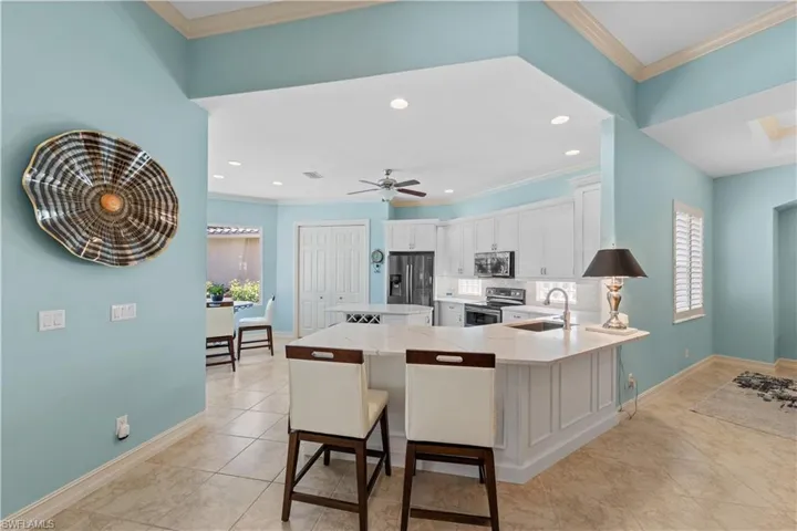 Kitchen with a breakfast bar area, a peninsula, ornamental molding, white cabinetry, and stainless steel appliances