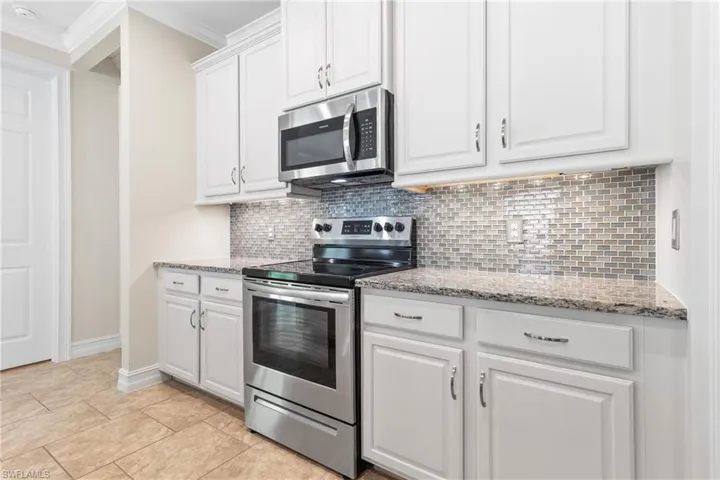 Kitchen with backsplash, crown molding, white cabinets, appliances with stainless steel finishes, and light stone counters