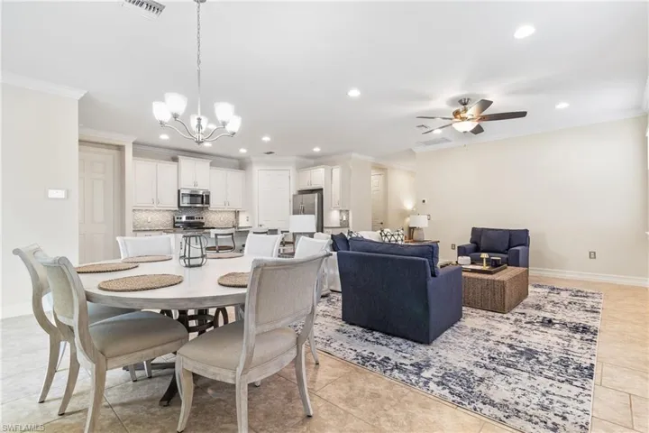 Dining space with crown molding, light tile patterned flooring, and ceiling fan with notable chandelier