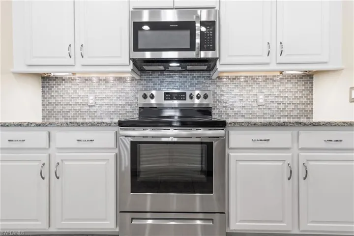 Kitchen featuring white cabinets, stainless steel appliances, light stone counters, and backsplash
