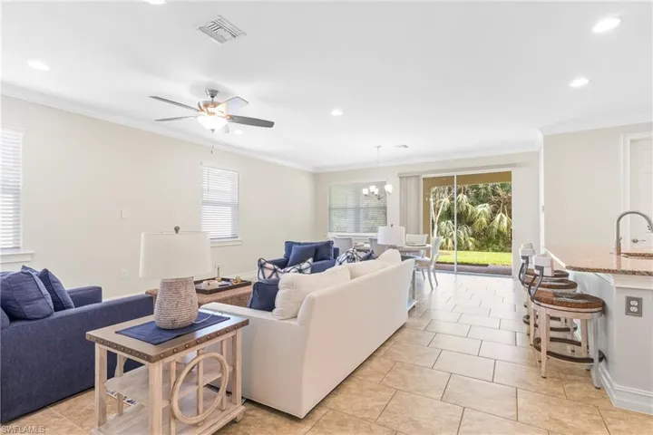 Tiled living room with crown molding, sink, and ceiling fan with notable chandelier