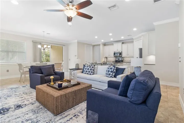 Tiled living room with ornamental molding, sink, and ceiling fan with notable chandelier