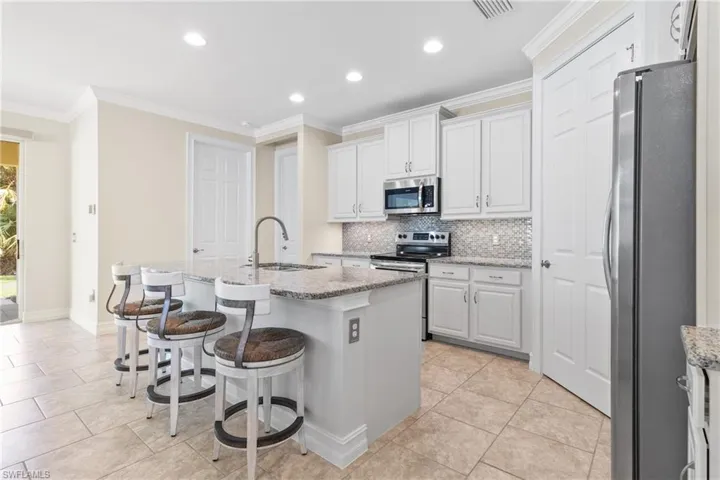 Kitchen featuring an island with sink, appliances with stainless steel finishes, white cabinetry, ornamental molding, and sink