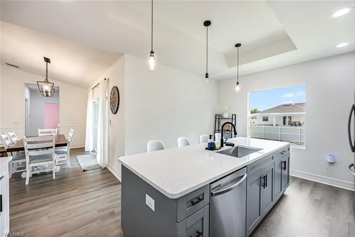 Kitchen featuring decorative light fixtures, stainless steel dishwasher, an island with sink, light stone countertops, and light wood-style floors