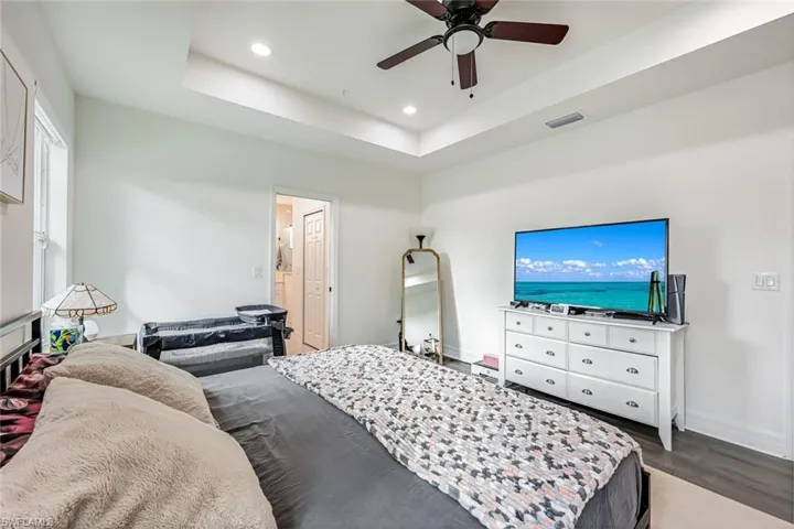 Bedroom with recessed lighting, a tray ceiling, a ceiling fan, and wood finished floors