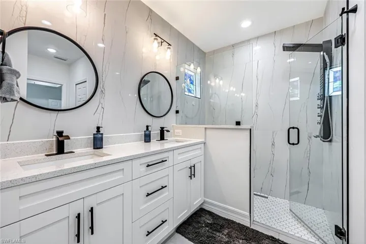 Full bathroom featuring double vanity, a marble finish shower, and recessed lighting