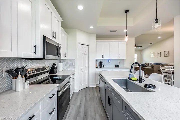Kitchen featuring stainless steel appliances, pendant lighting, two tone cabinets, light stone countertops, and light wood-type flooring