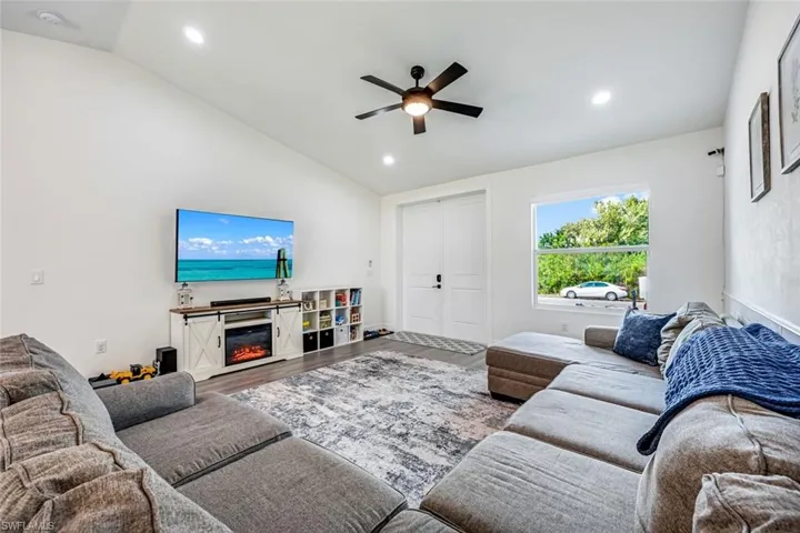 Living room featuring wood finished floors, lofted ceiling, a ceiling fan, recessed lighting, and a glass covered fireplace