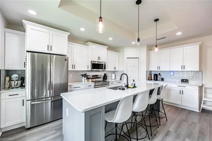Kitchen with stainless steel appliances, white cabinetry, a tray ceiling, light wood finished floors, and light stone counters