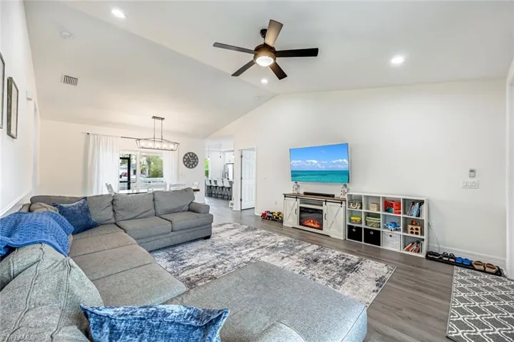 Living room featuring wood finished floors, ceiling fan, lofted ceiling, a glass covered fireplace, and recessed lighting