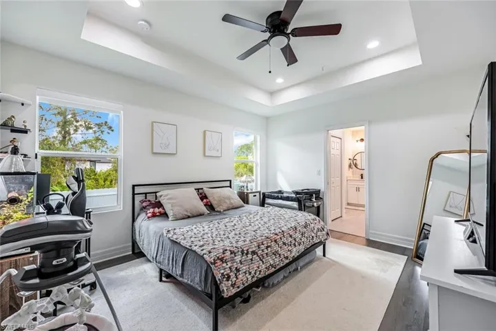 Bedroom featuring recessed lighting, wood finished floors, ceiling fan, a raised ceiling, and ensuite bath