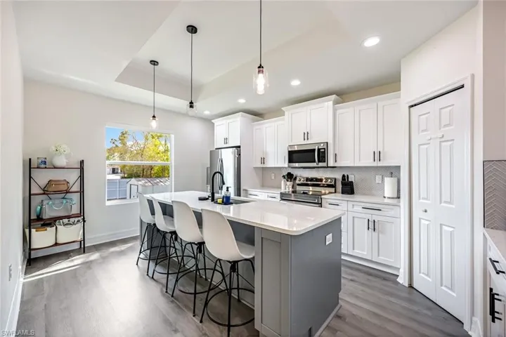 Two tone kitchen featuring a breakfast bar area, stainless steel appliances, an island with sink, decorative light fixtures, and dark wood finished floors