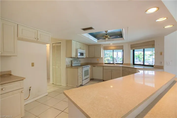Kitchen featuring white appliances, a peninsula, a raised ceiling, recessed lighting, and a sink