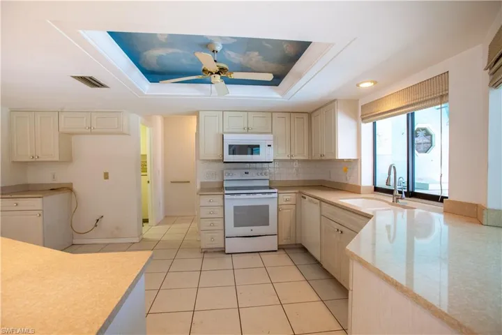 Kitchen with white appliances, a sink, light countertops, ceiling fan, and a tray ceiling