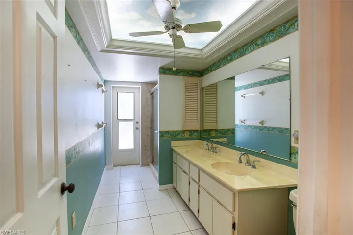 Bathroom featuring tile patterned flooring, a ceiling fan, a shower stall, double vanity, and toilet