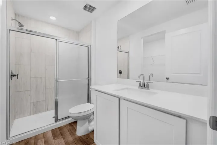 Modern bathroom featuring a walk-in shower with light tile surround, a single vanity with a white countertop, and wood-finish flooring