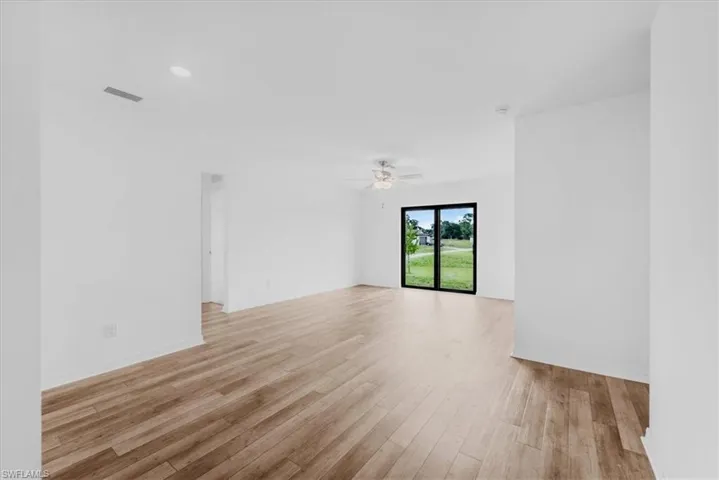 Spacious room featuring wood-finish flooring, white walls, and a ceiling fan
