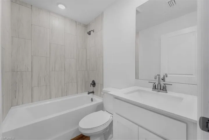 Bathroom featuring a white bathtub with light-toned tiled surround, a white vanity with an integrated sink, a large wall-mounted mirror, and recessed lighting