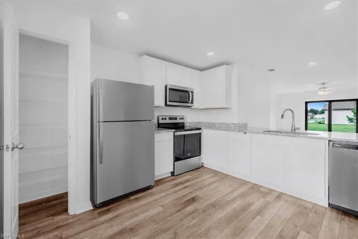 Modern kitchen with wood-finish flooring, white cabinetry, and granite countertops