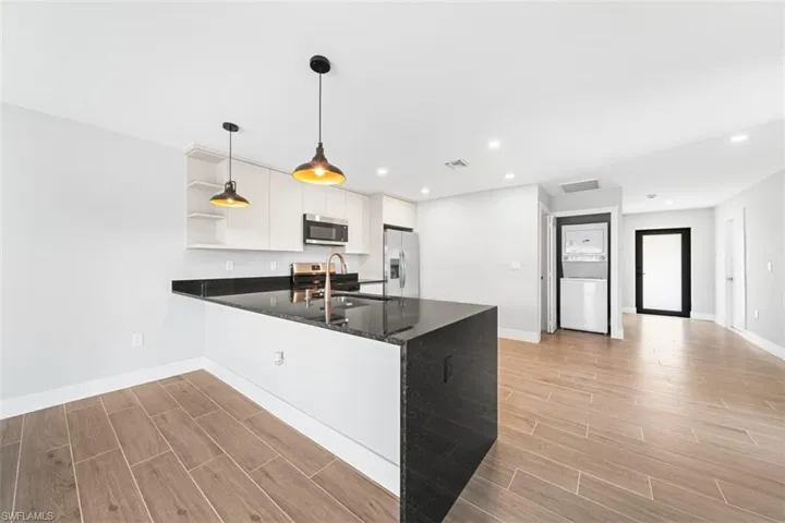 Kitchen featuring wood-finish flooring, a stone-surfaced kitchen island, flat-panel cabinetry, dual pendant lighting, and recessed ceiling lighting