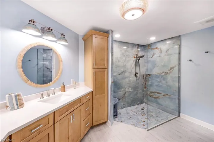 Primary Bathroom featuring a marble finish shower, vanity, and light wood-style floors