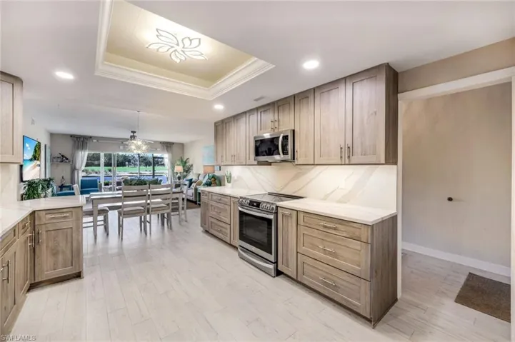 Kitchen featuring stainless steel appliances, recessed lighting, light wood-type flooring, a raised ceiling, and a ceiling fan