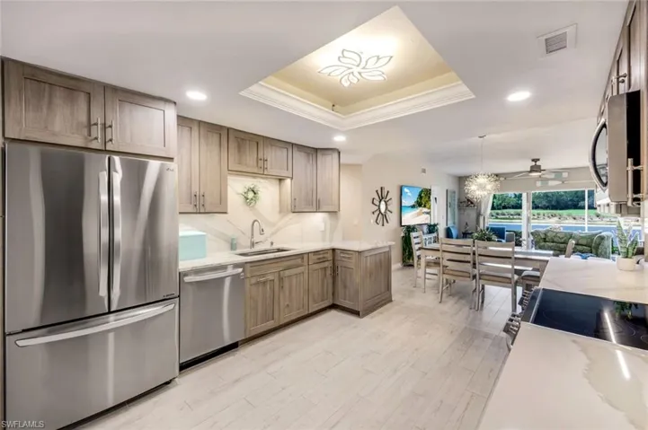 Kitchen featuring stainless steel appliances, a tray ceiling, ceiling fan, light stone countertops, and light wood-style flooring