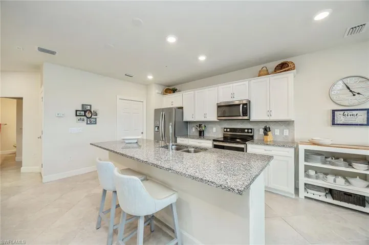 Kitchen with white cabinets, decorative backsplash, stainless steel appliances, light stone counters, and a breakfast bar