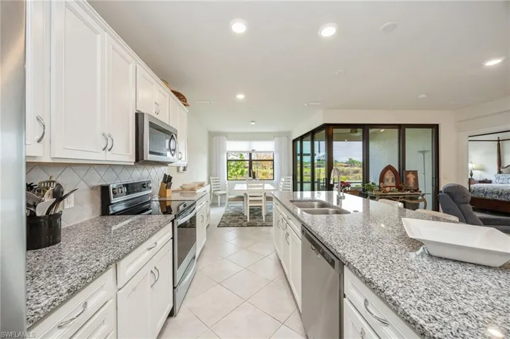 Kitchen with stainless steel appliances, white cabinets, light stone countertops, open floor plan, and backsplash