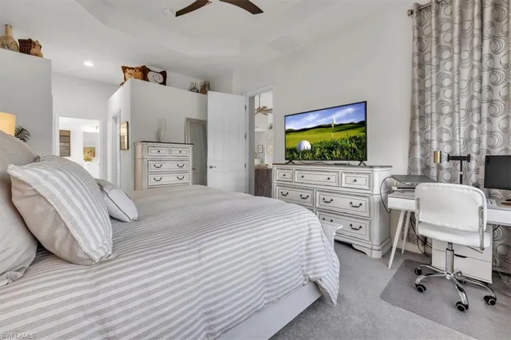 Bedroom featuring a desk, light colored carpet, connected bathroom, a ceiling fan, and a tray ceiling