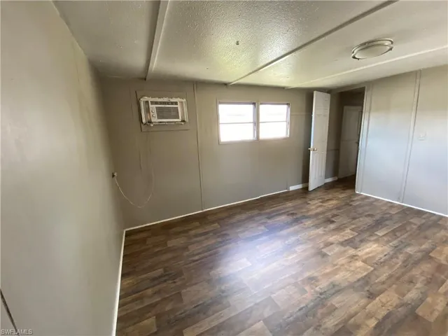 Unfurnished bedroom with a textured ceiling, dark wood-type flooring, and a wall unit AC