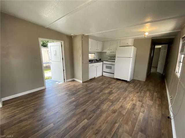 Kitchen featuring white cabinets, white appliances, a textured ceiling, dark wood-style flooring, and dark countertops