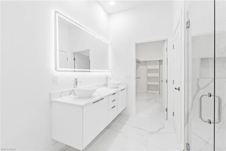 Bathroom featuring double vanity, light marble finish flooring, a marble finish shower, and a spacious closet