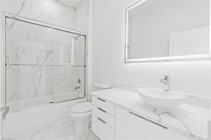 Full bathroom with vanity, light marble finish flooring, shower / bath combination with glass door, and a textured wall