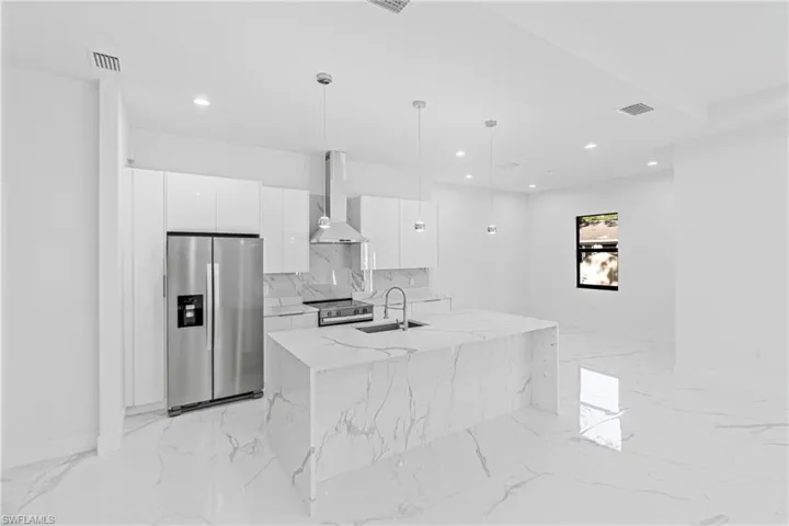 Kitchen with appliances with stainless steel finishes, white cabinetry, wall chimney exhaust hood, modern cabinets, and pendant lighting