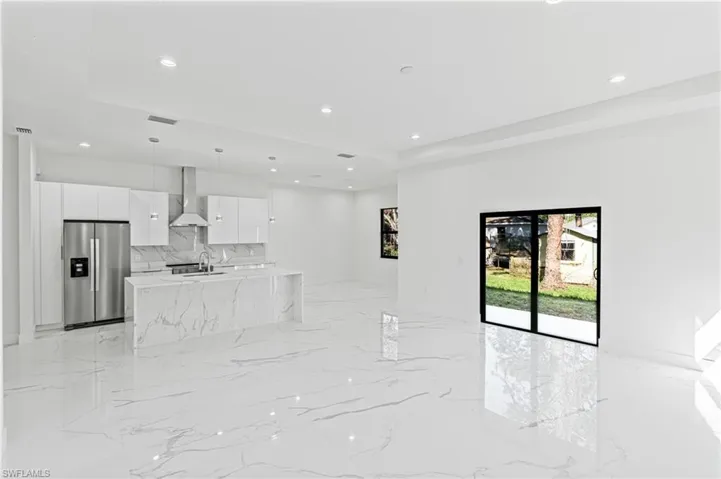 Kitchen featuring stainless steel refrigerator with ice dispenser, white cabinets, wall chimney exhaust hood, light stone counters, and modern cabinets