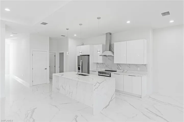 Kitchen with pendant lighting, wall chimney range hood, a center island with sink, stainless steel appliances, and modern cabinets