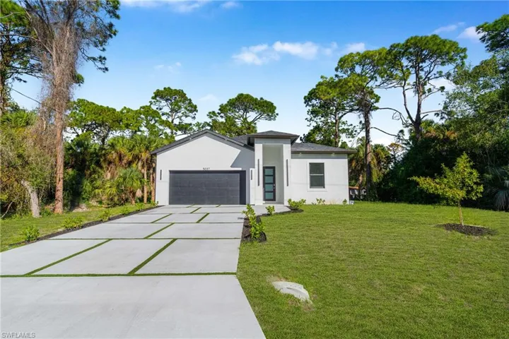 View of front of home featuring stucco siding, concrete driveway, a front yard, a garage, and view of scattered trees