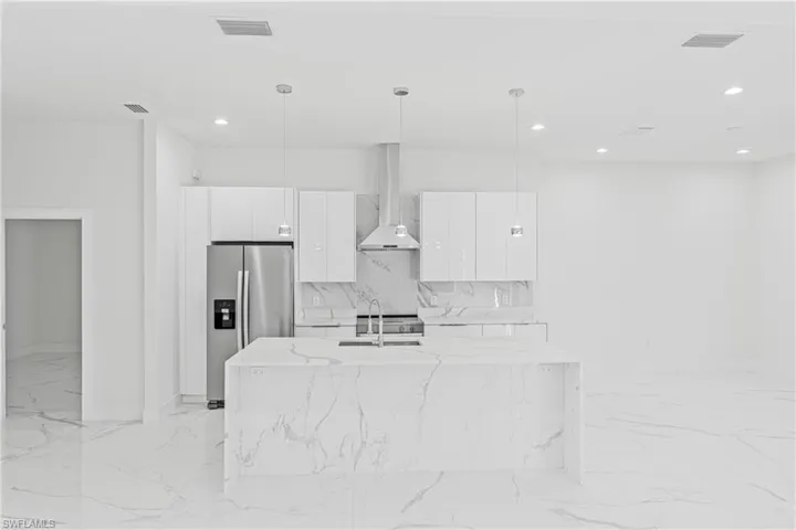 Kitchen featuring modern cabinets, stainless steel appliances, wall chimney range hood, pendant lighting, and white cabinets